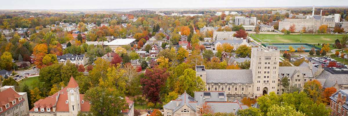 Aeriel shot of Indiana University Campus with buildings peaking through a sea of  with green and brown trees